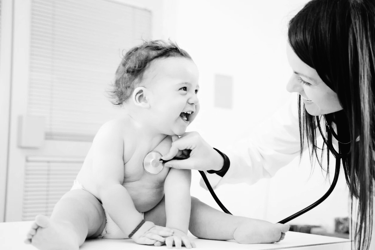 A smiling baby being examined with a stethoscope
